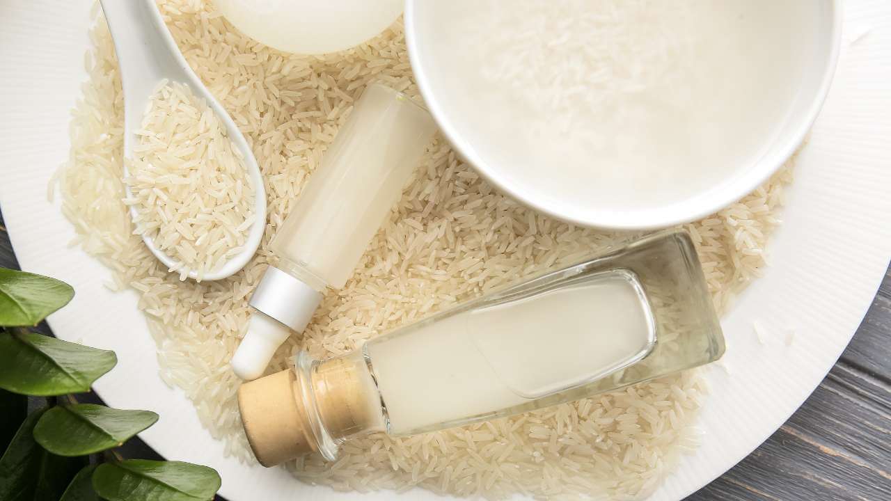 White porcelain plate full of rice with white spoon, fermented rice water in a serum bottle, clear jar, and bowl.