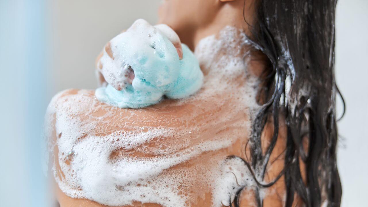 Woman using a pH balanced body wash for treating hyperpigmentation on her face and body as part of her shower routine.